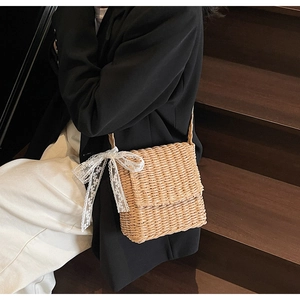 Detail of straw crossbody bag with white lace bow on woven texture shown on a model