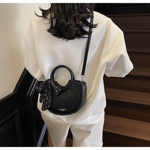 Détail du sac seau noir en cuir foulonné avec un foulard à pois et texte de mode