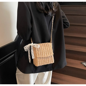 Detail of hand-woven straw crossbody bag with white lace bow on wooden stairs