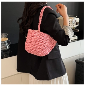 Close-up of pink straw bag with V-shaped weave pattern held by model in modern cafe