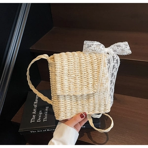Detail of handmade straw crossbody bag with white lace bow on wooden background