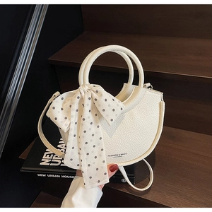 Détail d'un sac demi-lune en cuir blanc avec ruban à pois et poignée ronde rigide