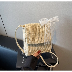 Detail of hand-woven straw phone bag with elegant white floral lace bow and slim strap