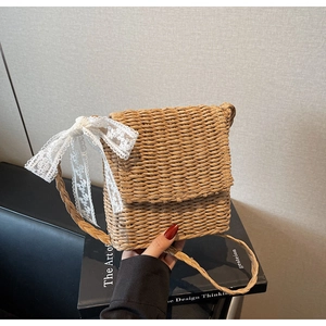 Detailed close-up of straw woven crossbody bag with elegant white lace bow decoration