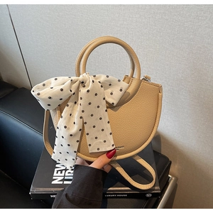 Détail du sac seau beige en cuir grainé avec un nœud à pois noirs sur la poignée