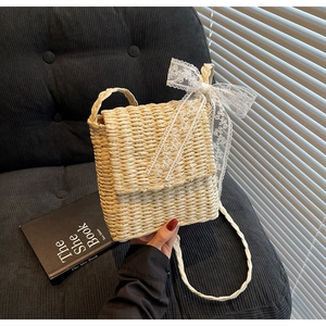 Detail of hand-woven straw crossbody bag with white lace bow decoration and strap