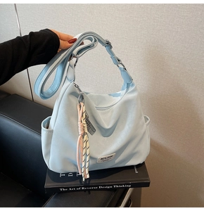 Detail view of light blue tote bag with woven tassel charm and adjustable strap