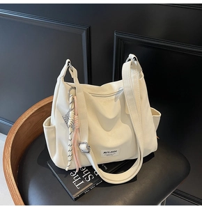 Detail of white PU leather tote bag with Mulaidi logo and colorful woven pendant