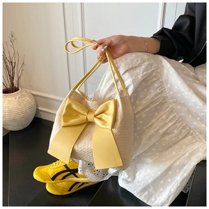 Détail du cabas en paille crème avec un grand nœud en satin jaune et des anses d'épaule