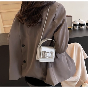 Detail of a silver mini bag with metallic texture, bow clasp, and thin chain shoulder strap