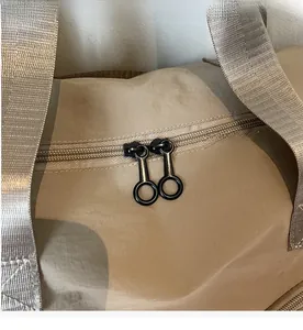 Close-up of dual black circular metal zippers and water-resistant nylon on beige travel bag