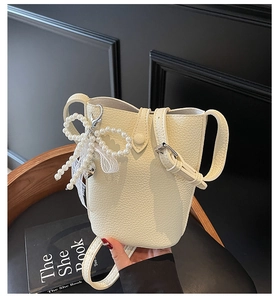 Détail du sac seau en cuir crème texturé avec pendentif nœud en perles élégant