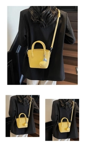 Detail view of bright yellow bucket bag with heart pendant on black suit background