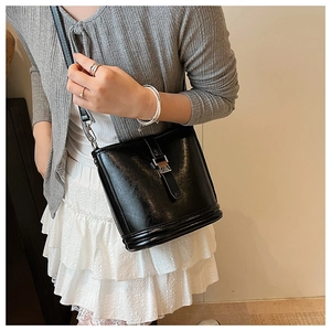Détail d'un sac seau en cuir noir avec boucle métallique porté par un mannequin élégant
