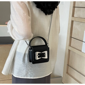 Detail view of the mini black leather crossbody bag featuring a large silver metal bow buckle
