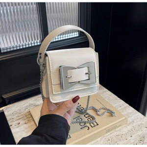 Detail of white mini handbag with silver metal bow clasp and chain strap on marble
