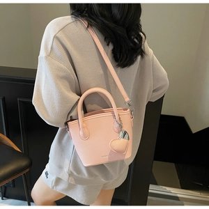 Pink lychee textured bucket bag with heart charm shown as a stylish crossbody detail