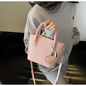 Pink lychee texture bucket bag with a decorative metal heart charm and crossbody strap