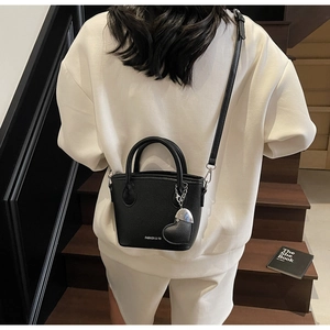 Detail of black lychee grain leather bucket bag with heart pendant and crossbody strap