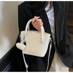 Detail of off-white lychee pattern leather bucket bag with heart pendant and shoulder strap