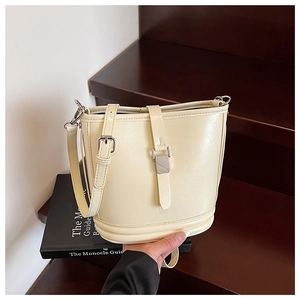 Détail du sac seau crème avec bandoulière réglable et boucle en métal argenté sur bois