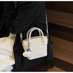 Detail of white lychee leather bucket bag with heart charm and brand text on strap