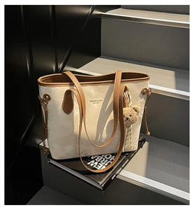 Detail of a beige tote bag with brown straps and a cute plush bear charm on a step