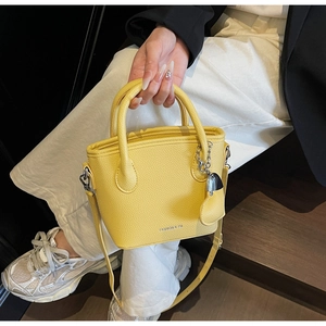 Close-up of bright yellow litchi pattern bucket bag with a heart metal charm and logo detail