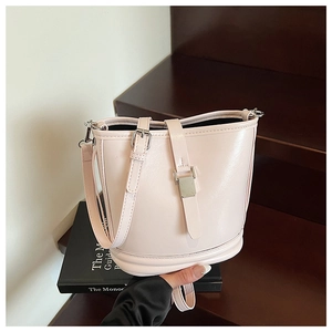 Détail du sac seau en cuir rose pâle avec boucle argentée sur des escaliers