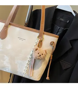 Detail of minimalist cream tote bag with brown straps and cute teddy bear charm