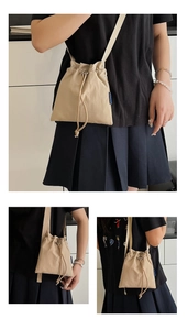 Detail of a beige nylon drawstring bucket bag showing adjustable strap and texture