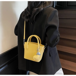 Close-up of bright yellow litchi texture bucket bag with heart pendant and silver chain