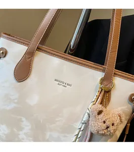 Detail of white marble pattern tote bag with brown leather handles and plush bear charm