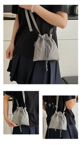 Close-up detail of grey nylon drawstring crossbody bag with brand woven label and texture