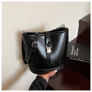Gros plan du sac seau en cuir noir brillant avec boucle argentée sur des marches en bois