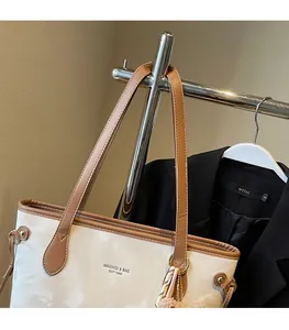 Detail of soft cream tote bag with brown leather handles and brand logo engraving