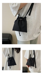 Detail view of black nylon drawstring bucket bag with adjustable strap and blue woven label