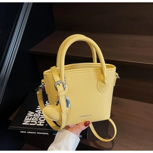 Close-up of bright yellow lychee texture bucket bag with heart pendant on wooden steps