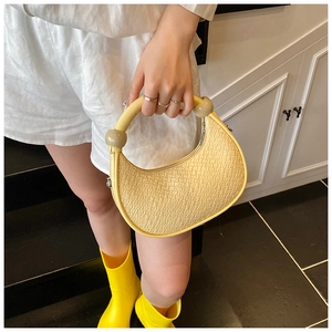 Detailed view of yellow woven texture crescent bag with round handle and spherical accents