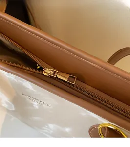 Detailed close-up of golden metal zipper and gold branding on white leather tote bag