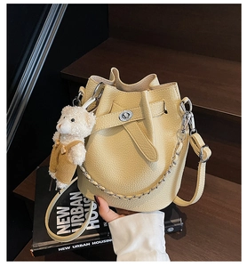 Nahaufnahme der gelben Eimer-Tasche mit Litschiprägung, Bärenanhänger und Metallkette