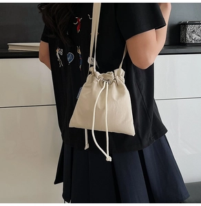 Detail view of beige nylon drawstring crossbody bag worn by model in a casual setting