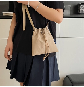 Detail of minimalist beige nylon crossbody bag with drawstring closure on model