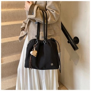 Detail of black drawstring tote bag featuring a baseball charm and silver clover logo charm