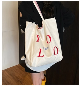 Close-up of YOLO red embroidery and striped handle on a white canvas tote bag