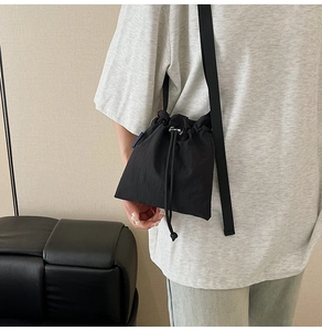 Detail of black drawstring nylon crossbody bag with adjustable strap and brand tag