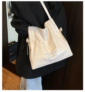Detailed close-up of cream PU leather tote bag featuring blue bow embroidery and ribbon