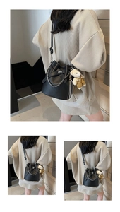 Detailansicht einer schwarzen Eimer-Handtasche mit Litschi-Muster und süßem Bären-Anhänger