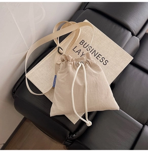 Detail of a beige nylon crossbody phone bag with drawstring closure and blue label