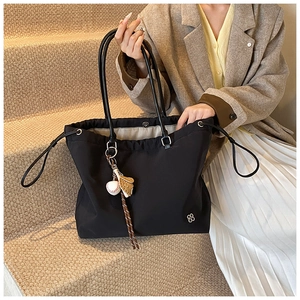 Close-up of black tote bag with clover logo and baseball glove charm on steps